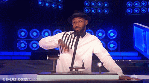 A Man In A White Shirt And Black Hat Stands In Front Of A Microphone With The Words Game Of Games Behind Him GIF