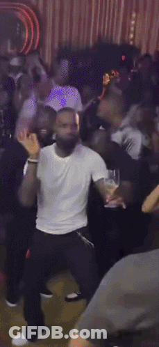 A Man In A White Shirt And Black Pants Is Dancing In A Crowd GIF
