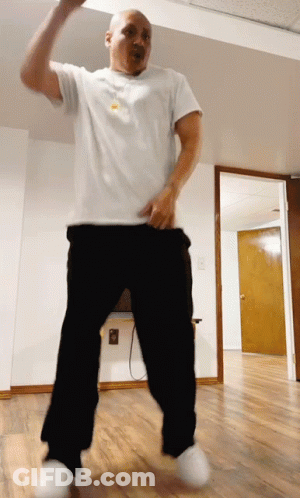 A Man In A White Shirt And Black Pants Is Dancing In An Empty Room GIF