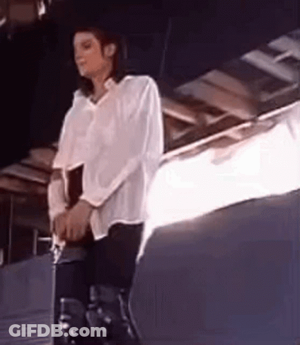 A Man In A White Shirt And Black Pants Is Sitting On A Stool . GIF