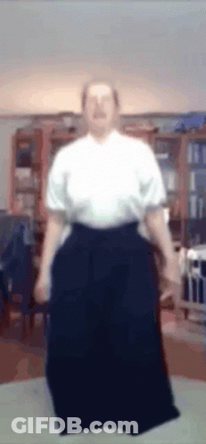 A Man In A White Shirt And Black Pants Is Standing In A Room GIF