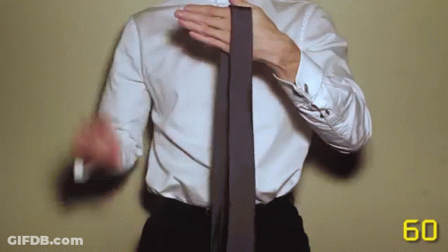A Man In A White Shirt And Black Pants Is Tying A Tie GIF