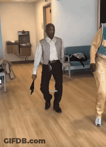 A Man In A White Shirt And Black Pants Is Walking In A Hallway With A Watermark That Says Shills1987 GIF