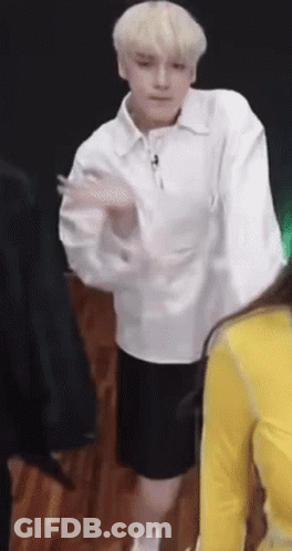 A Man In A White Shirt And Black Shorts Is Dancing In Front Of A Group Of People . GIF