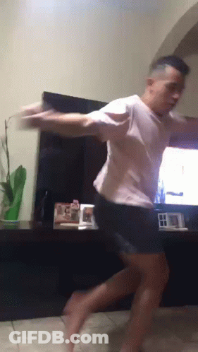 A Man In A White Shirt And Black Shorts Is Dancing In Front Of A Tv GIF