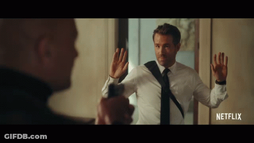 A Man In A White Shirt And Black Tie Is Holding A Gun In Front Of Another Man In A Netflix Advertisement GIF