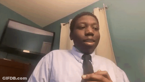 A Man In A White Shirt And Black Tie Is Standing In Front Of A Flat Screen Tv GIF