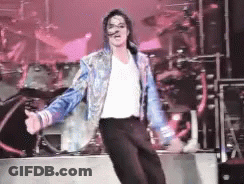 A Man In A White Shirt And Blue Jacket Is Dancing On Stage GIF