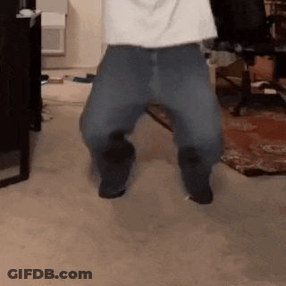 A Man In A White Shirt And Blue Jeans Is Jumping In The Air In A Living Room . GIF