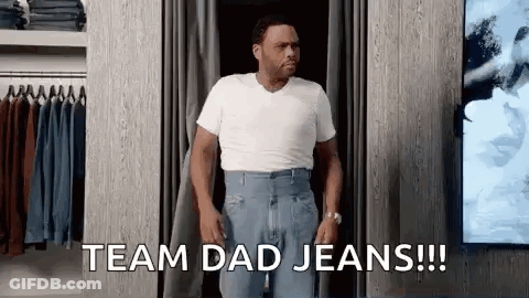 A Man In A White Shirt And Blue Jeans Is Standing In A Dressing Room . GIF