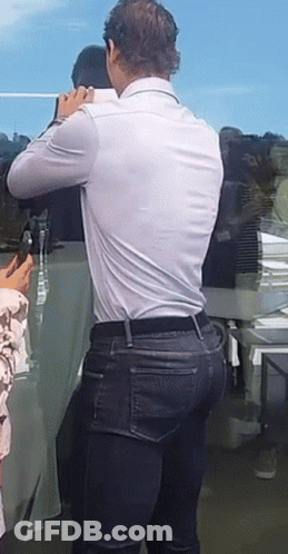 A Man In A White Shirt And Blue Jeans Is Standing In Front Of A Table GIF
