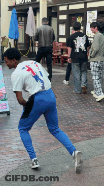 A Man In A White Shirt And Blue Pants Stands On A Sidewalk In Front Of A Neko Store GIF