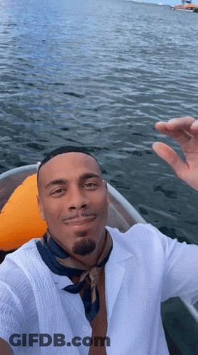 A Man In A White Shirt And Blue Scarf Is Taking A Selfie In A Boat In The Water GIF