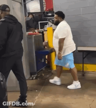 A Man In A White Shirt And Blue Shorts Is Walking Through A Room GIF