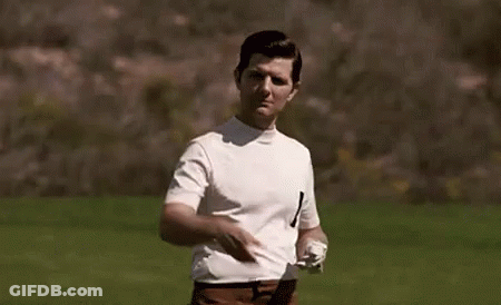 A Man In A White Shirt And Brown Pants Is Standing In A Field Holding A Golf Club . GIF