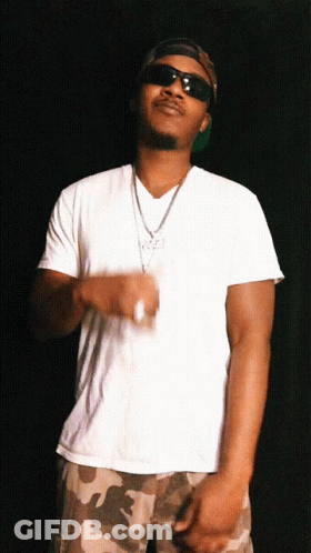 A Man In A White Shirt And Camo Shorts Is Wearing Sunglasses And A Necklace GIF