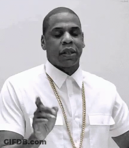 A Man In A White Shirt And Gold Chain Is Pointing At The Camera . GIF
