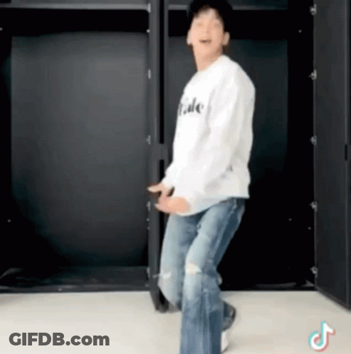 A Man In A White Shirt And Jeans Is Dancing In Front Of A Black Wall . GIF