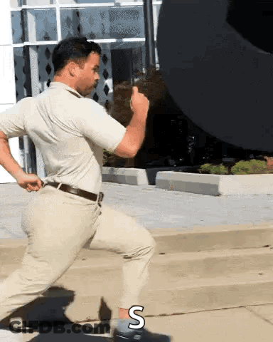 A Man In A White Shirt And Khaki Pants Is Running Down The Street GIF
