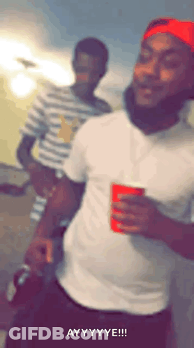 A Man In A White Shirt And Red Hat Is Holding A Red Cup And Making A Funny Face . GIF