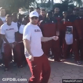 A Man In A White Shirt And Red Pants Is Dancing In Front Of A Crowd Of People . GIF