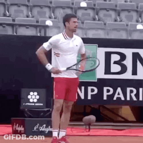 A Man In A White Shirt And Red Shorts Is Holding A Tennis Racket . GIF