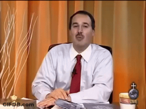 A Man In A White Shirt And Red Tie Is Sitting At A Desk In Front Of A Curtain . GIF