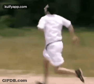 A Man In A White Shirt And Shorts Is Running On A Dirt Road . GIF