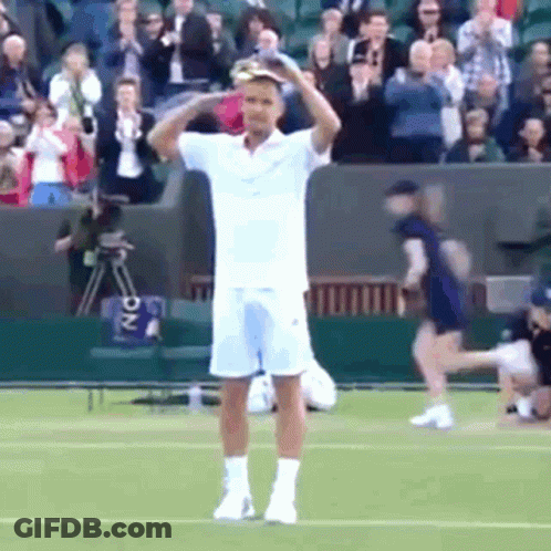 A Man In A White Shirt And Shorts Is Standing On A Tennis Court Holding His Head . GIF