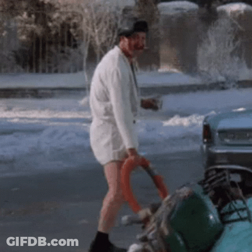 A Man In A White Shirt And Shorts Is Walking Down A Snowy Street GIF