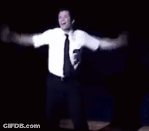A Man In A White Shirt And Tie Is Dancing On A Stage In The Dark . GIF