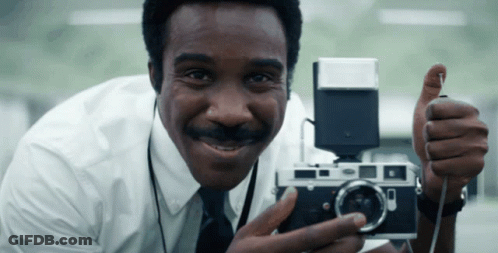 A Man In A White Shirt And Tie Is Holding A Camera And Giving A Thumbs Up GIF