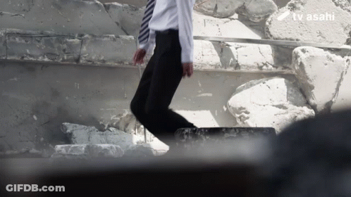 A Man In A White Shirt And Tie Is Jumping Over A Pile Of Rocks With The Tv Asahi Logo In The Background GIF