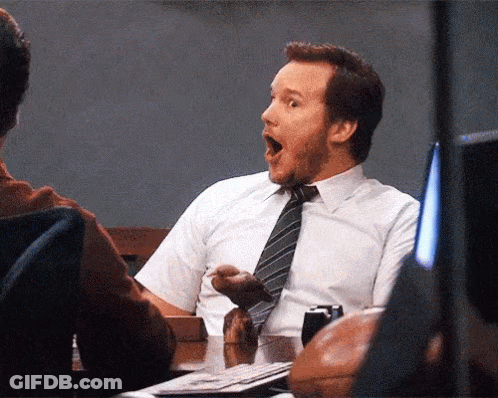 A Man In A White Shirt And Tie Is Sitting At A Desk With His Mouth Open GIF