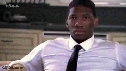 A Man In A White Shirt And Tie Is Sitting On A Couch In A Kitchen . GIF