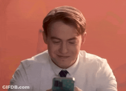 A Man In A White Shirt And Tie Is Smiling And Looking At His Phone GIF