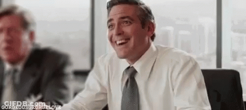 A Man In A White Shirt And Tie Is Smiling While Sitting At A Table In An Office . GIF