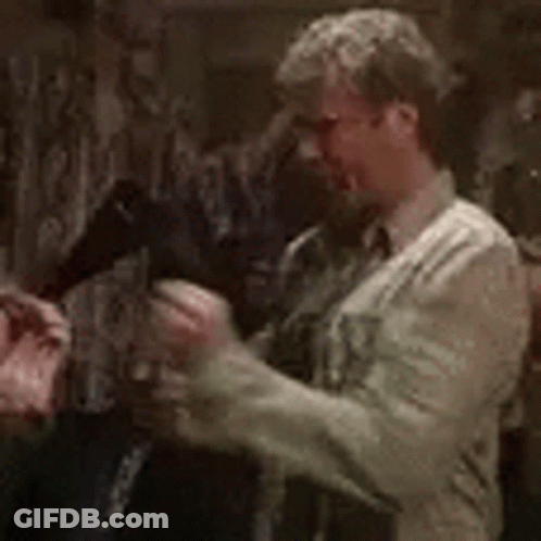 A Man In A White Shirt And Tie Is Standing In A Dark Room Holding A Gun . GIF
