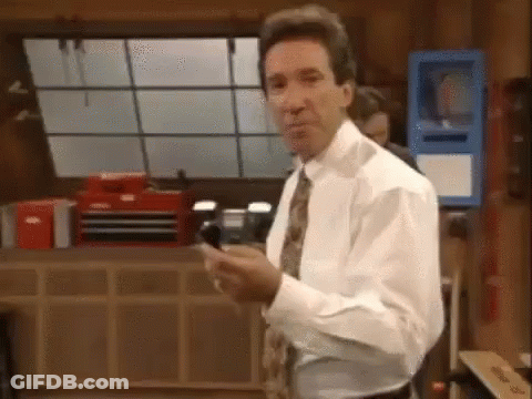 A Man In A White Shirt And Tie Is Standing In A Room Holding A Cell Phone In His Hand . GIF