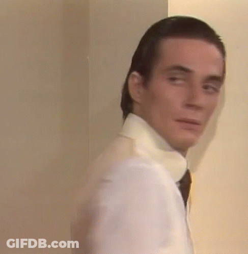 A Man In A White Shirt And Tie Is Standing Next To A Wall And Looking At The Camera . GIF