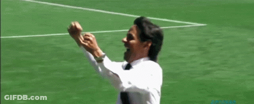 A Man In A White Shirt And Tie Is Standing On A Soccer Field With His Fist In The Air GIF