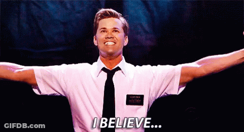 A Man In A White Shirt And Tie Is Standing On A Stage With His Arms Outstretched And Says I Believe . GIF