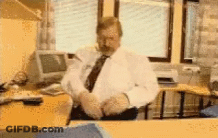 A Man In A White Shirt And Tie Sits At A Desk GIF