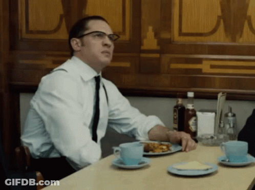 A Man In A White Shirt And Tie Sits At A Table With Plates Of Food GIF