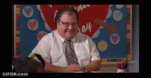 A Man In A White Shirt And Tie Sits In Front Of A Bulletin Board That Says I Love You GIF