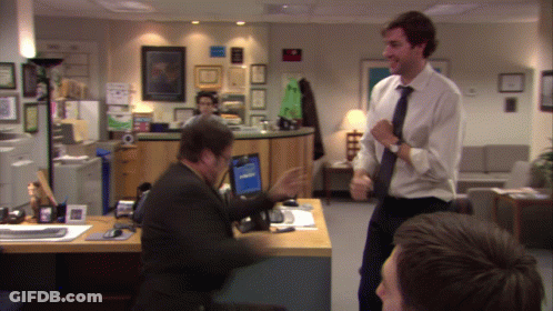A Man In A White Shirt And Tie Stands In Front Of A Man Sitting At A Desk GIF
