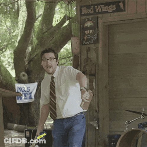 A Man In A White Shirt And Tie Stands In Front Of A Sign That Says Red Wings GIF