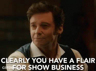 A Man In A White Shirt And Vest Is Smiling And Says `` Clearly You Have A Flair For Show Business '' . GIF