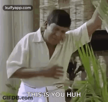 A Man In A White Shirt And White Pants Is Standing Next To A Plant And Talking To It . GIF
