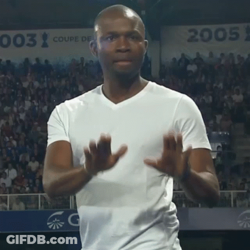 A Man In A White Shirt Applauds In Front Of A Sign That Says 003 GIF